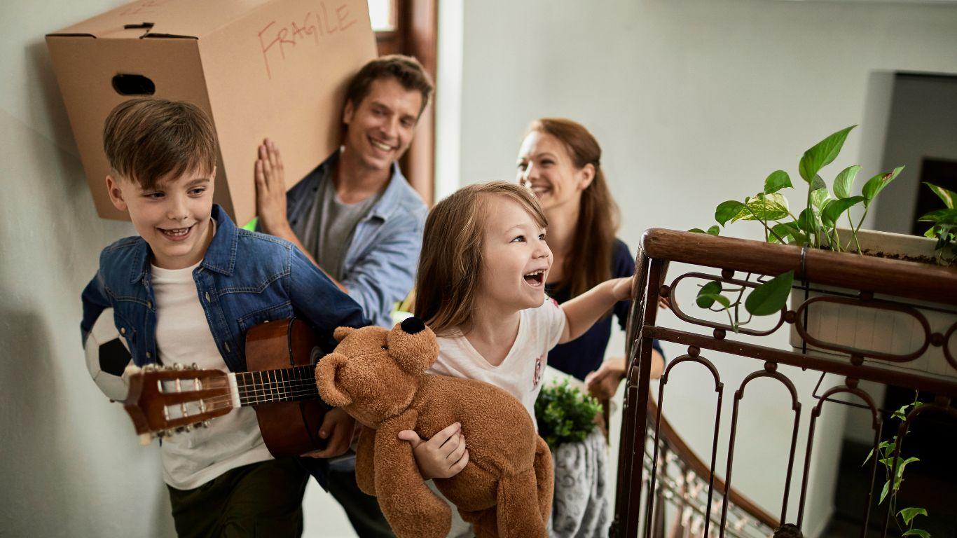 Family walking up stairs into their new house with kids holding a teddy with a smile on their face after securing a new mortgage